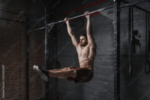 Crossfit athlete doing abs exercise on horizontal bar at the gym. Handsome man doing functional training workout. Practicing calisthenics.