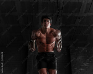 Young shirtless muscle athlete doing ring dips in the gym. Professional calisthenics athlete working out